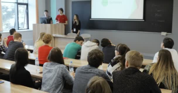 Vista desde atrás de un grupo de estudiantes en un aula, escuchando mientras su maestro imparte una conferencia. vista posterior — Vídeos de Stock