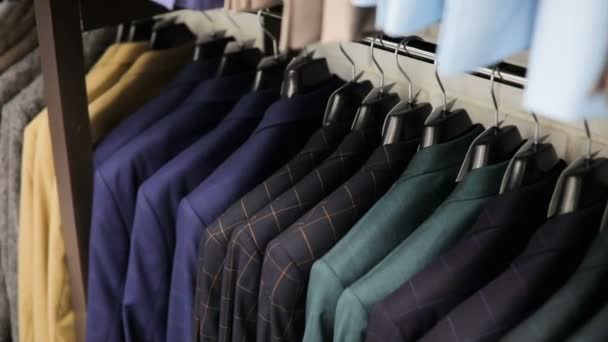 A fila de homens ajusta jaquetas em cabides. Coleção de novas roupas bonitas penduradas em cabides em uma loja — Vídeo de Stock