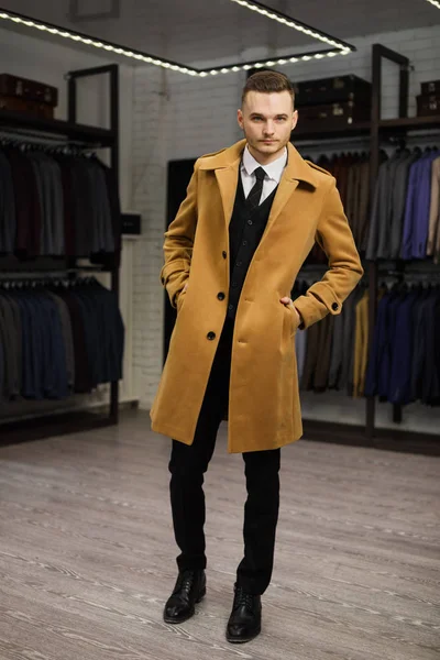 英俊的男子站在西装店时髦的富人穿着昂贵的衣服摆在室内 — 图库照片