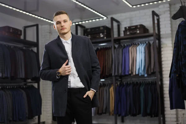 Красивый мужчина стоит в магазине костюмов модный богатый мужчина одетый в дорогую одежду позируя в помещении — стоковое фото