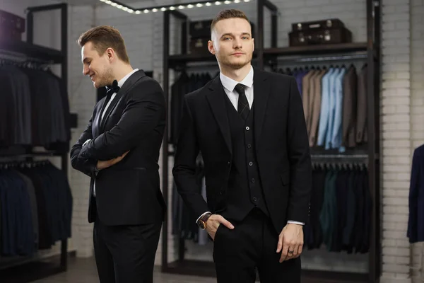 Dva gay přátelé v klasické vesty proti řadě obleků v obchodě — Stock fotografie