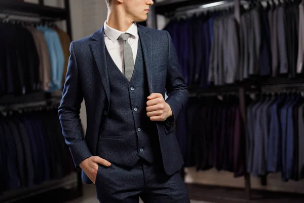 Vendita, shopping, moda, stile e concetto di persone - elegante giovane uomo che sceglie e prova giacca in centro commerciale o negozio di abbigliamento — Foto Stock