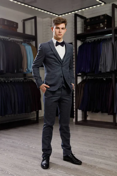 Empresario en chaleco clásico contra hilera de trajes en tienda. Un hombre joven y elegante con chaqueta. Está en la sala de exposición, probándose ropa, posando. Publicidad foto — Foto de Stock