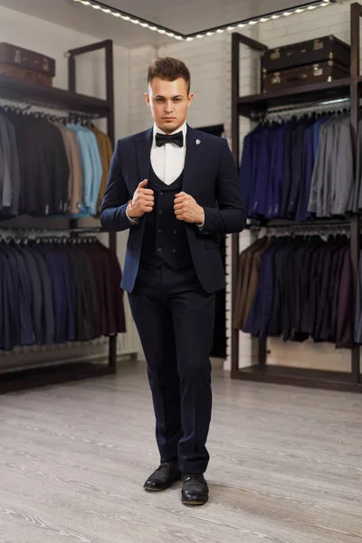 Businessman in classic vest against row of suits in shop. A young stylish man in a jacket. It is in the showroom, trying on clothes, posing. Advertising photo — Stock Photo, Image