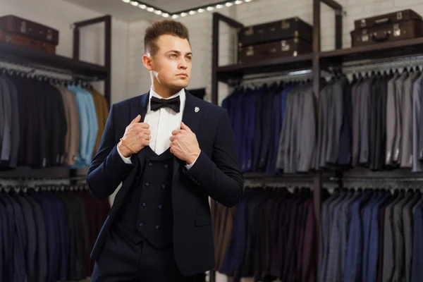 Joven en chaleco clásico contra la fila de trajes en la tienda — Foto de Stock