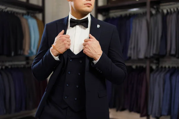 Cliente es un tipo elegante probándose un traje en una tienda de espejos. En el fondo trajes clásicos y chaquetas — Foto de Stock