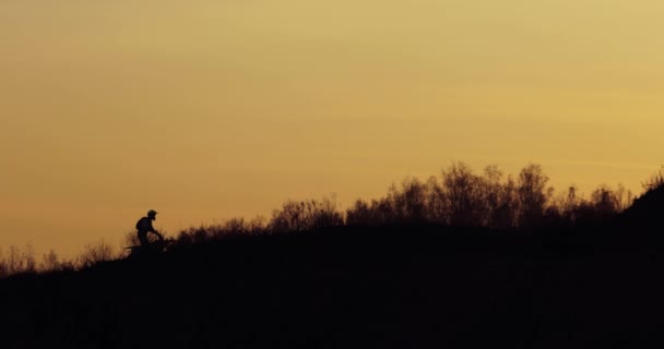 Silhueta de motociclista está andando off road em montanhas ao pôr do sol no escuro . — Vídeo de Stock