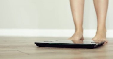 Yalınayak kadın evde terazinin üzerinde duruyor, ayaklar kapalı..