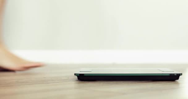 Barefooted woman is standing on scales weightning at home, feet closeup. — Stock Video