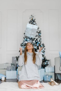 Mutlu genç kadın yılbaşı ağacının yanına hediyeler fırlatıyor.