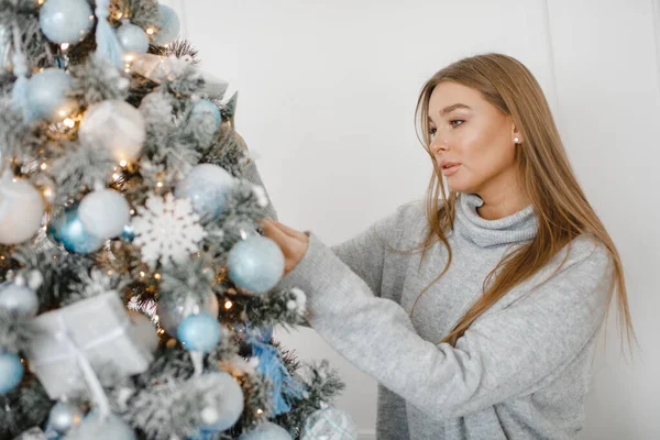 Una chica en un suéter decora un árbol de Navidad. Concepto de Año Nuevo . — Foto de Stock