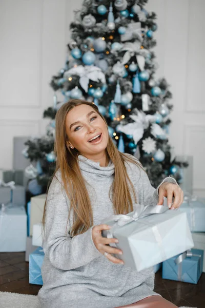 Navidad, x-mas, invierno, concepto de felicidad - mujer sonriente con muchas cajas de regalo. Chica abre un regalo en el fondo del árbol de Navidad. feliz joven celebrando la Navidad — Foto de Stock