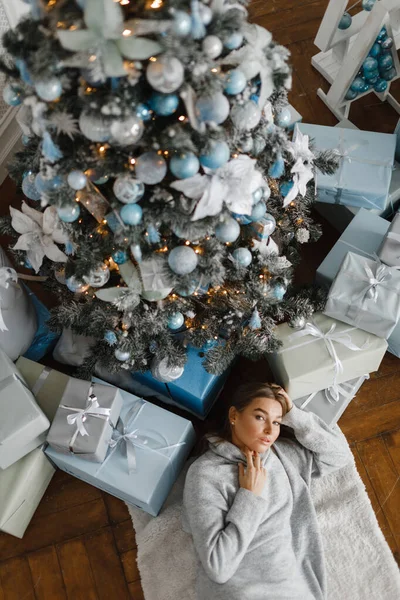 Hermosa chica cerca del árbol de Navidad está rodeado de regalos, vista superior. chica se regocija en regalos — Foto de Stock