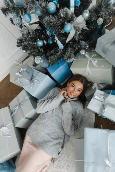Hermosa chica cerca del árbol de Navidad está rodeado de regalos, vista superior. chica se regocija en regalos — Foto de Stock
