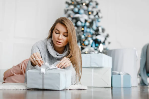 Hermosa chica cerca del árbol de Navidad está rodeado de regalos, desempaca regalos — Foto de Stock