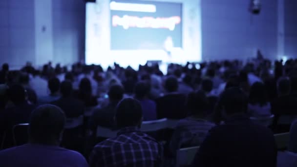 Hombre en el escenario hablando y mostrando la presentación en pantalla en un gran auditorio . — Vídeo de stock