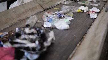 Yeniden kullanım için geri dönüşüm fabrikasında taşınan taşıma bandı üzerindeki çöpleri sıralayan işçiler.
