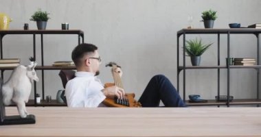 Erkek ofis çalışanı gitar çalıyor ve sandalyede dönüyor. Keyfini çıkarıyor..