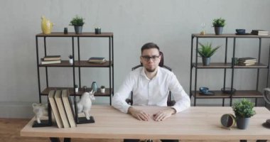 Gözlüklü genç bir ofis çalışanı masada oturmuş kameraya bakıyor..