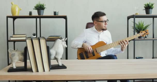 Ο νεαρός παίζει κιθάρα και το απολαμβάνει καθισμένος στο γραφείο στο διάλειμμα.. — Αρχείο Βίντεο