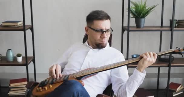 Junger Mann spielt Gitarre und genießt es, in der Pause im Büro zu sitzen. — Stockvideo