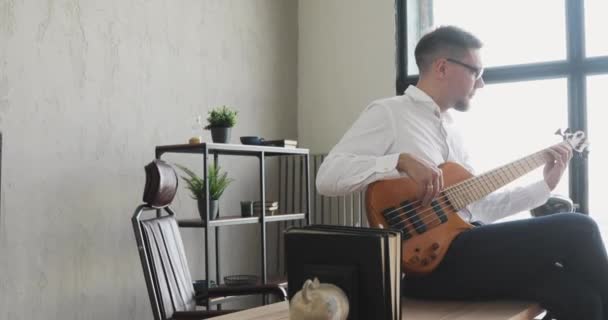 商务人员喜欢坐在办公室桌子上弹奏吉他，相机在动. — 图库视频影像