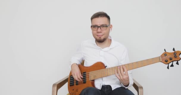 Retrato del hombre guitarrista tocando la guitarra sentado en sillón en casa . — Vídeo de stock