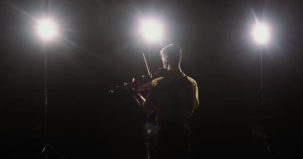 Silhouette of man violinist plays violin in light of spotlights, back view. — Stock Video