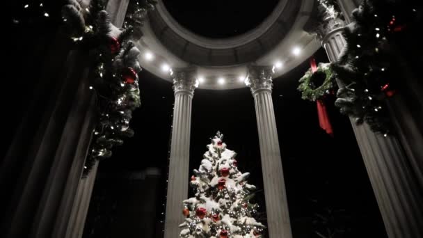 Árbol de Navidad decorado en mirador con columnas cubiertas de nieve en la noche santa . — Vídeos de Stock