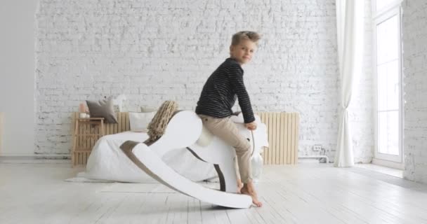 Petit garçon enfant se balance sur cheval à bascule dans la crèche jouer dans le temps libre . — Video