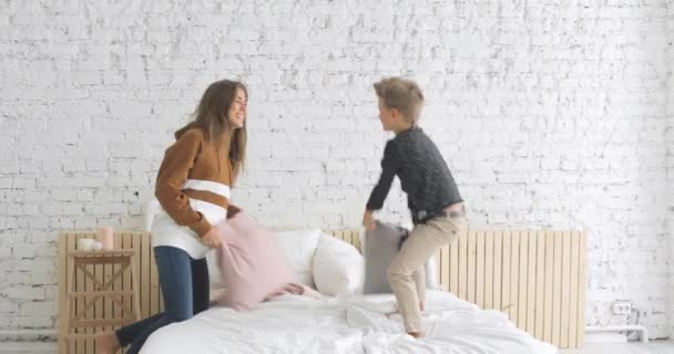 Happy family mother and son having funny pillow fight on bed in nursery at home. — Stock Video