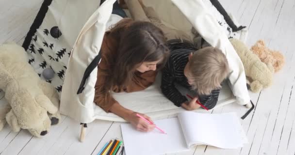 Matka a syn malují tužky na albu společně ležící v týpí v jeslích. — Stock video