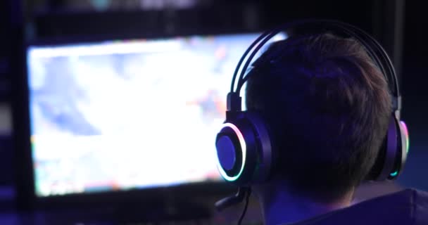 Homem gamer no fone de ouvido está jogando jogo de vídeo olhando para a tela no escuro, visão traseira . — Vídeo de Stock