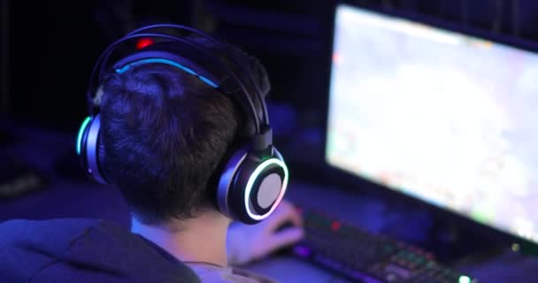Muž hráč ve sluchátkách hraje videohry při pohledu na obrazovku ve tmě, pohled zezadu. — Stock video