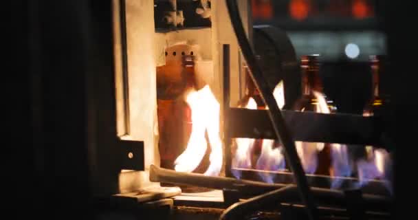 Glazen flessen bewegen langs transportband lijn vallen onder open vlam te verharden glas. — Stockvideo