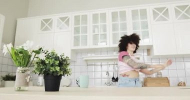 Happy young woman with curly hairs is dancing and singing in kitchen at home.