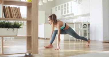Sporty young woman is making lunge exercise warming body in living room at home.