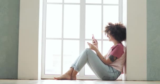 Ragazza sta effettuando il pagamento online carta di credito utilizzando smartphone seduto vicino alla finestra . — Video Stock