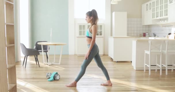 Mujer joven deportiva está haciendo embestida en postura de yoga en las piernas estiradas en casa . — Vídeo de stock