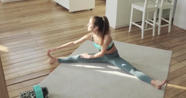 Sporty young woman making stretching exercise sitting at home leans to leg. — 비디오