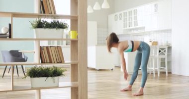 Sporty young woman is making slopes warming body before training at home.