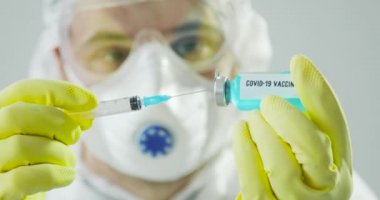 Koruyucu giysiler içindeki doktorun portresi şırıngayı koronavirüs aşısıyla dolduruyor..