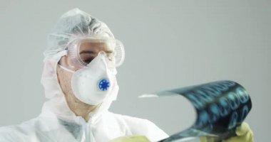 Koruyucu giysiler içindeki portre doktoru beyin tomografisi görüntüsüne bakıyor..