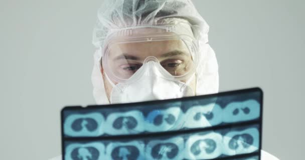 Lekarz w ubraniach ochronnych uczący się obrazu tomografii komputerowej mózgu podczas epidemii covid-19. — Wideo stockowe
