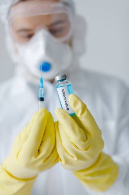 Koruyucu giysiler içindeki doktorun portresi şırıngayı koronavirüs aşısıyla dolduruyor..