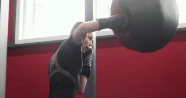 Eldivenli boksör spor salonunda boks yaparken kum torbasına yumruk atıyor..