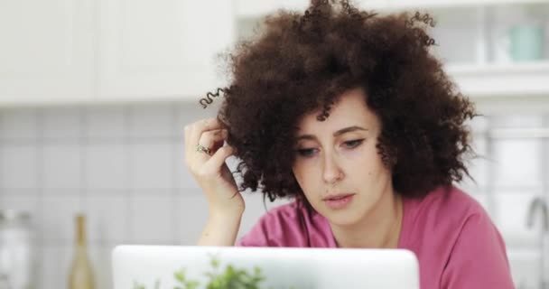 Портрет молодої жінки фрілансера з кучерявим волоссям, що працює на ноутбуці на кухні . — стокове відео