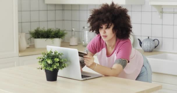 Menina fazendo pagamento on-line segurando cartão bancário usando laptop moderno em casa . — Vídeo de Stock