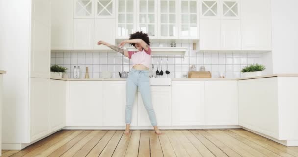 Ładna młoda kobieta z kręconymi włosami tańczy i śpiewa w kuchni w domu. — Wideo stockowe