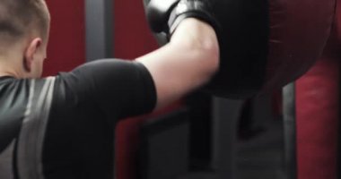 Eldivenli boksör spor salonunda boks torbasını yumrukluyor..